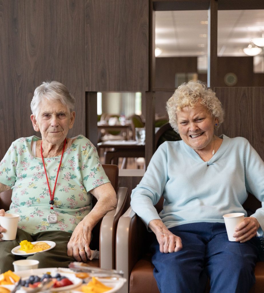 two smiling residents sitting with assorted snacks